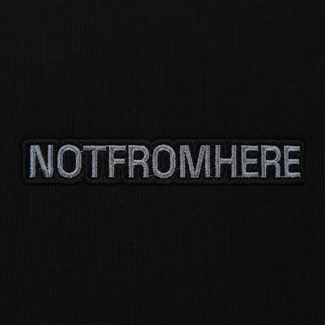 Close-up NOTFROMHERE logo detail on black oversized t-shirt